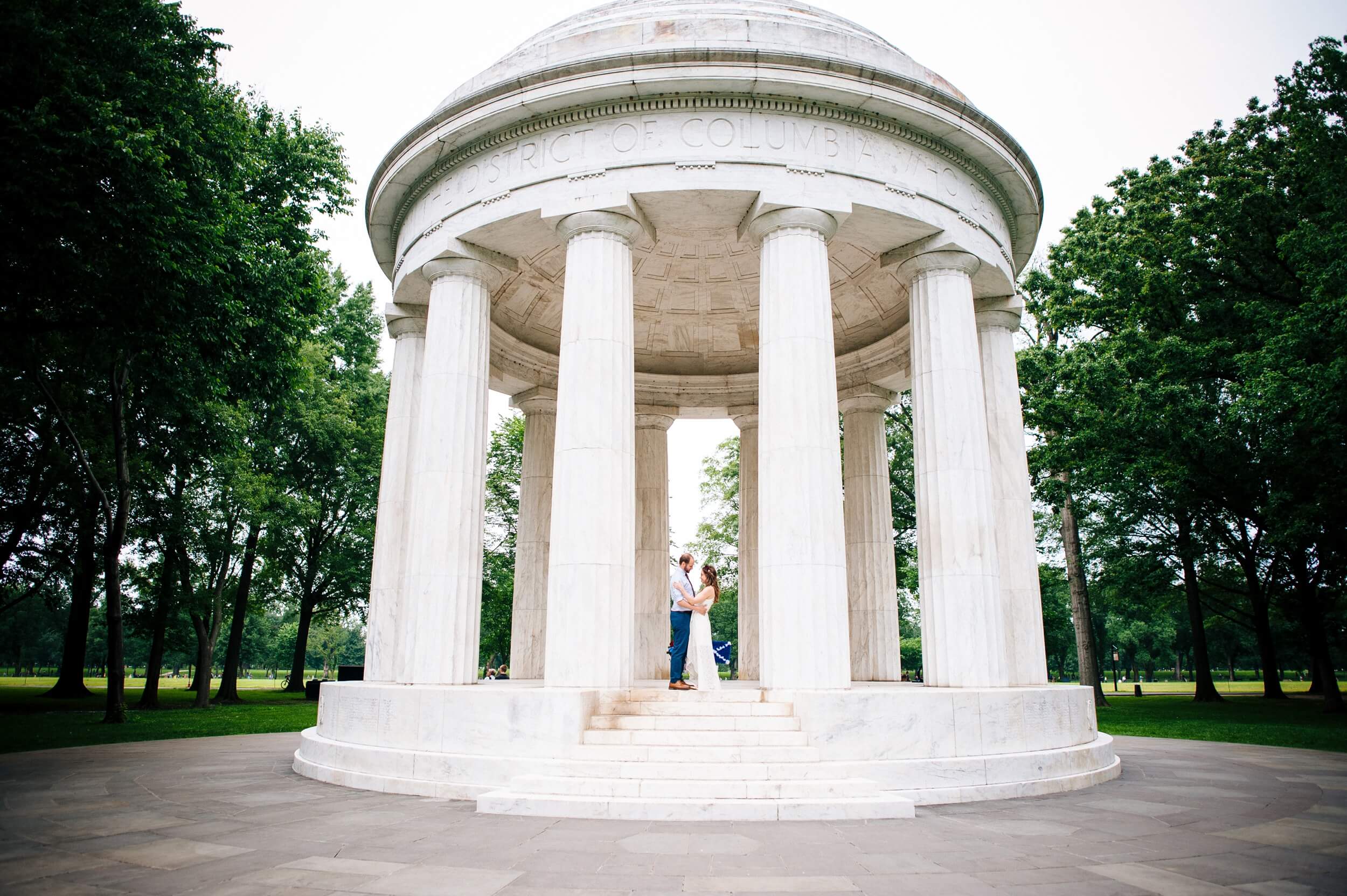 wide angle photo of just married couple standing under the dc war memorial