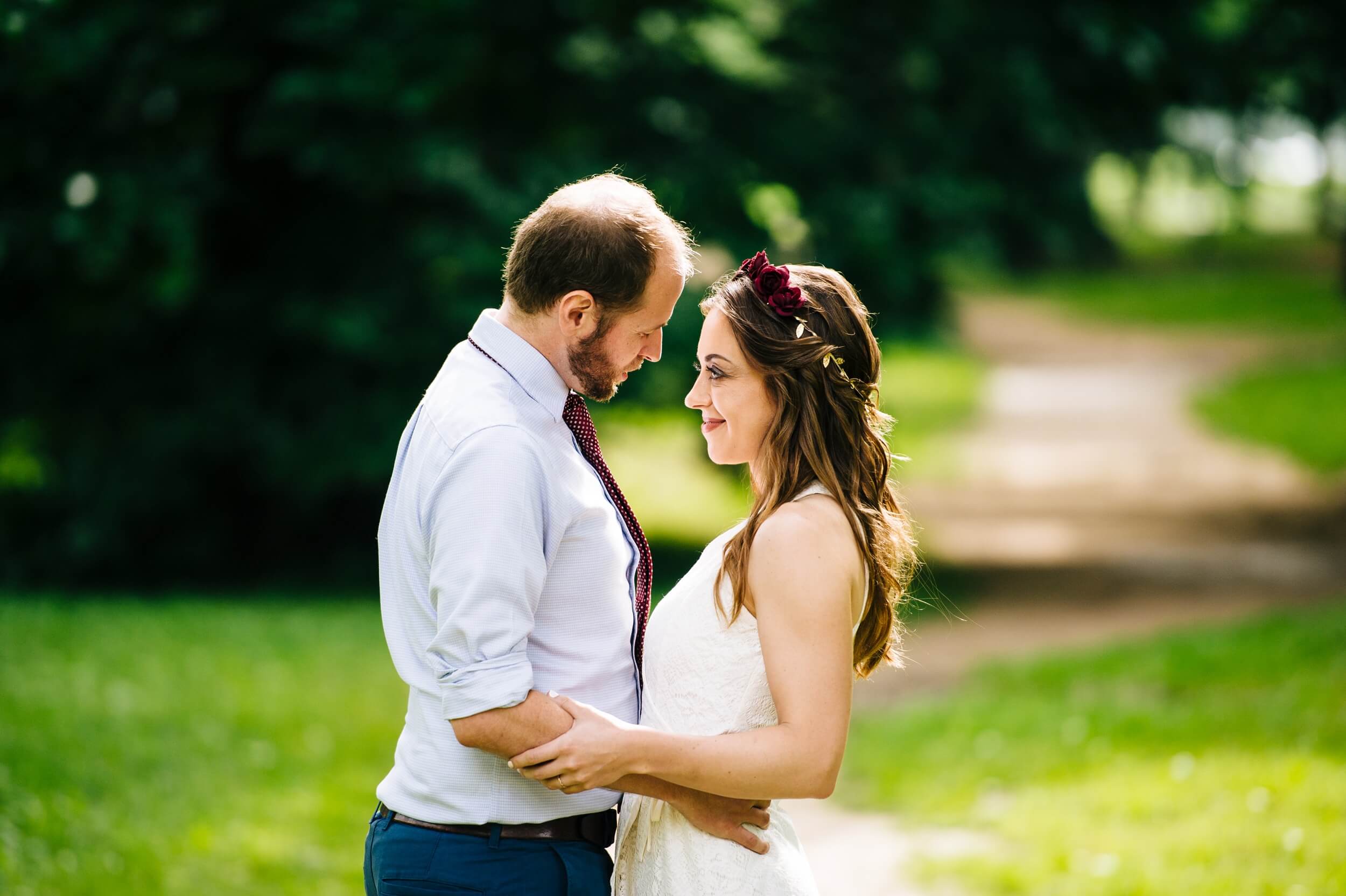 couple embracing and looking into each others eyes with sunlight and greenery behind